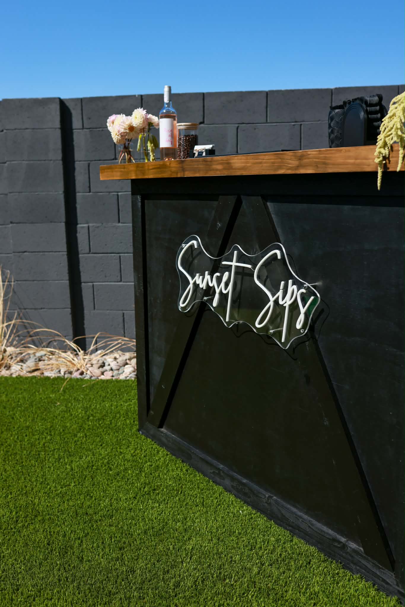 Black Sunset Sips mobile bar with a wood countertop and illuminated logo outdoors