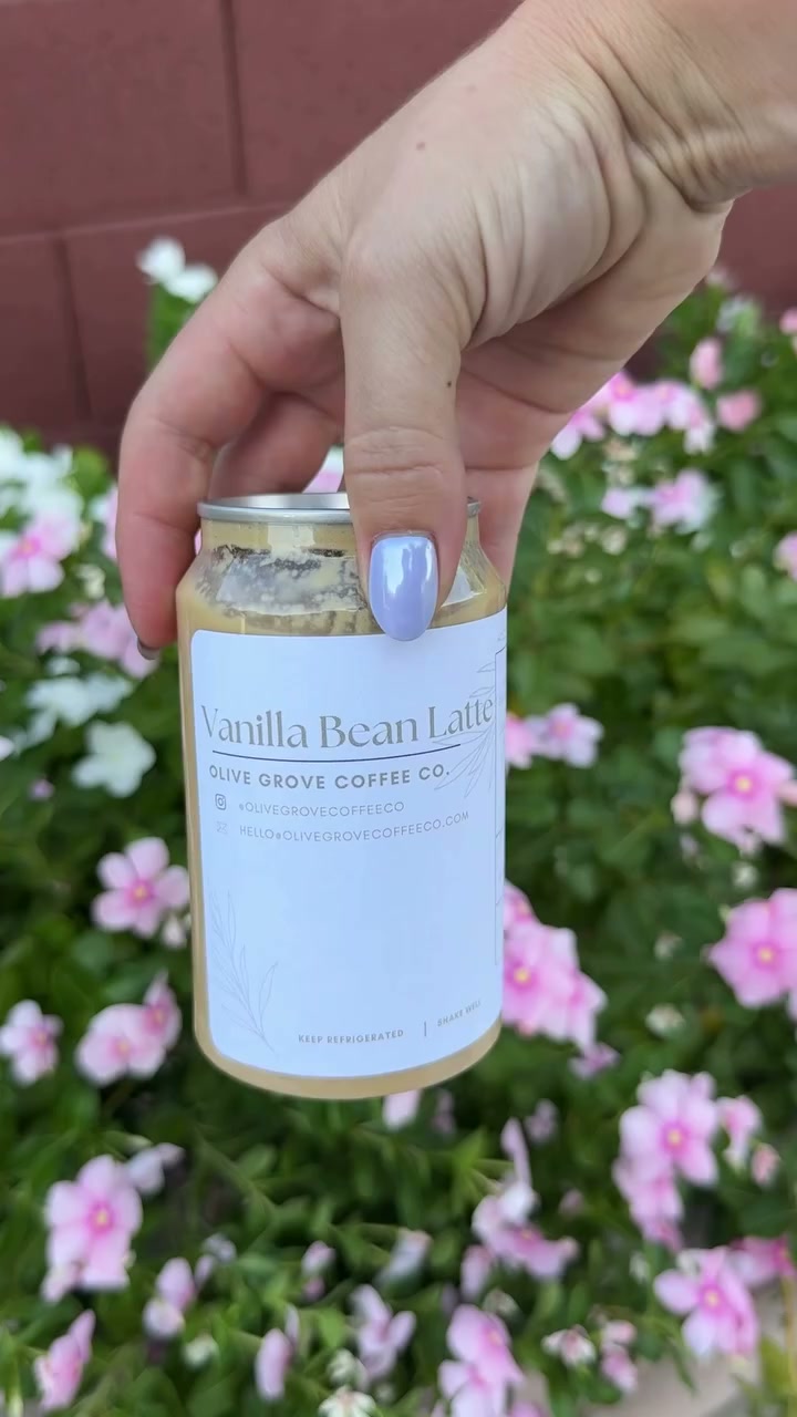 A labeled Olive Grove latte bottle held up against olive trees