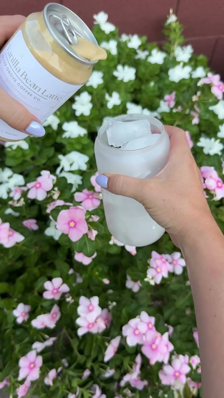A cream-colored bottle of Olive Grove coffee being filled with a fresh espresso pour, garnished with flowers